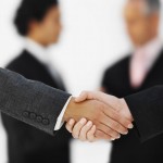 Close-up of the hands of two businesswomen shaking hands with two businessmen in background